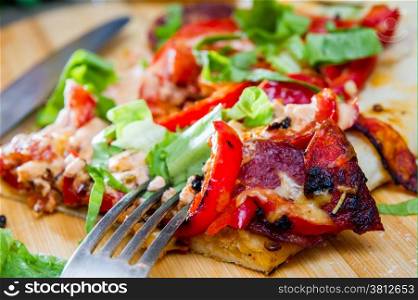 slice of pizza with peppers, bacon and herbs on a round wooden board