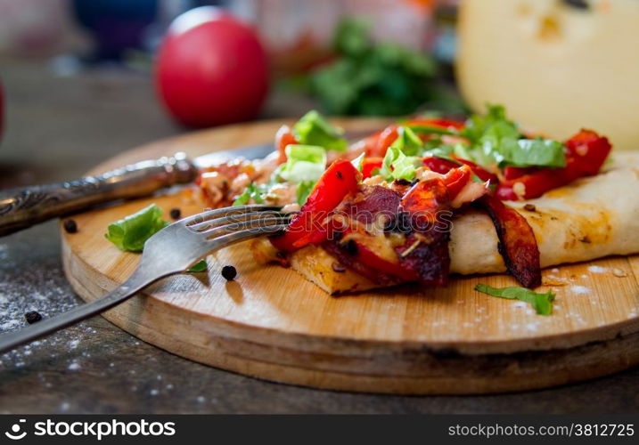 slice of pizza with peppers, bacon and herbs on a round wooden board