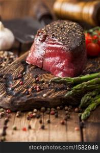 Slice of Raw Beef Topside Joint with Salt and Pepper on wooden chopping board with tomatoes garlic and asparagus tips on wood kitchen table.