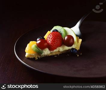 Slice of strawberry, kiwi, orange and grape tart on plate