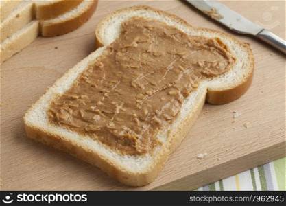 Slice of white bread with peanut butteron a wooden cutting board