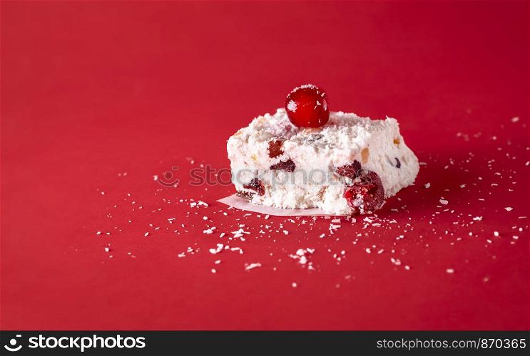Slice of white Christmas cake with coconut, dried fruit, and cherries, on a red background. Australian traditional sweet food. Winter holiday dessert