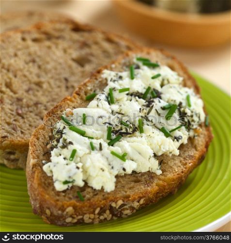 Slice of wholegrain bread spread with goat cheese with herbs with chives on top (Selective Focus, Focus one third into the cheese)