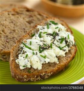 Slice of wholegrain bread spread with goat cheese with herbs with chives on top (Selective Focus, Focus one third into the cheese)