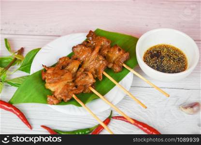 Slice pork skewer sticks grilled on banana leaf on white plate with sauce chilli garlic / Grilled pork thai asian street food style