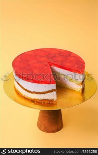 Sliced Birthday Cake decorated with red jelly and strawberries on top on the wooden cake stand. Beautiful sponge cake with whipped cream. Yellow background. Copy space. Food photography for recipe.