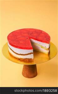 Sliced Birthday Cake decorated with red jelly and strawberries on top on the wooden cake stand. Beautiful sponge cake with whipped cream. Yellow background. Copy space. Food photography for recipe.