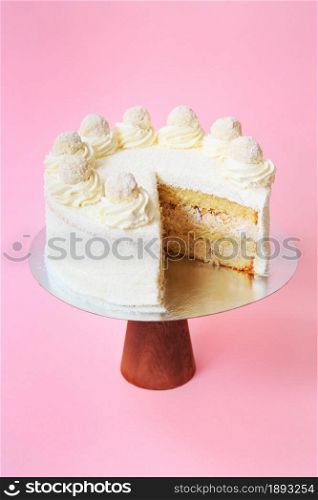 Sliced Birthday cake on the wooden cake stand. Beautiful white sponge cake with whipped cream. Pink background. Copy space. Food photography for recipe.