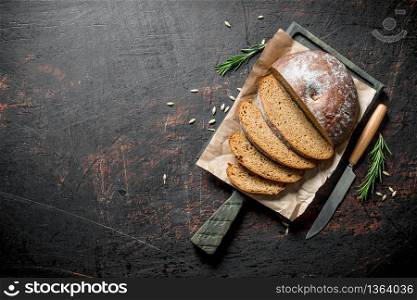 Sliced bread on a cutting Board with a knife and rosemary. On dark rustic background. Sliced bread on a cutting Board with a knife and rosemary.