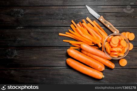 Sliced carrots in a bowl with a knife. On black wooden background. Sliced carrots in a bowl with a knife.