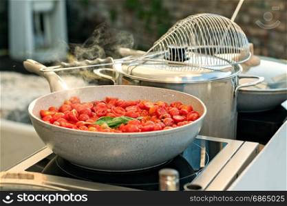 Sliced cherry tomatoes with basil cooking on a saucepan. Cherry tomatoes on a saucepan