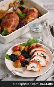 Sliced ??chicken breast stuffed with goat cheese with spinach, wrapped in prosciutto, with a side dish of baked potatoes, tomato and dried prunes