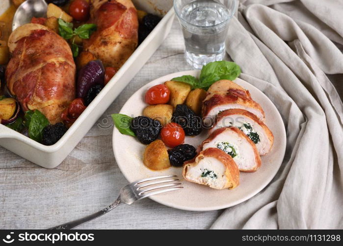 Sliced ??chicken breast stuffed with goat cheese with spinach, wrapped in prosciutto, with a side dish of baked potatoes, tomato and dried prunes