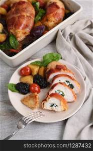 Sliced ??chicken breast stuffed with goat cheese with spinach, wrapped in prosciutto, with a side dish of baked potatoes, tomato and dried prunes