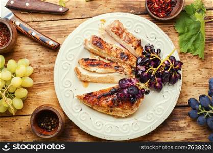 Sliced chicken breast with grapes on rural wooden table. Sliced grilled chicken breast