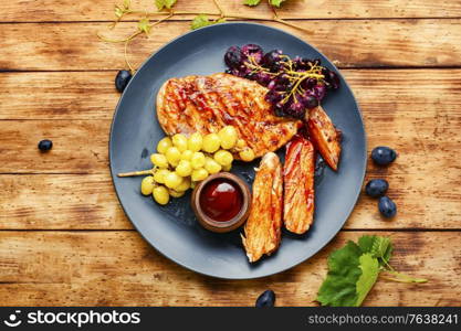 Sliced chicken breast with grapes on rural wooden table. Sliced grilled chicken breast