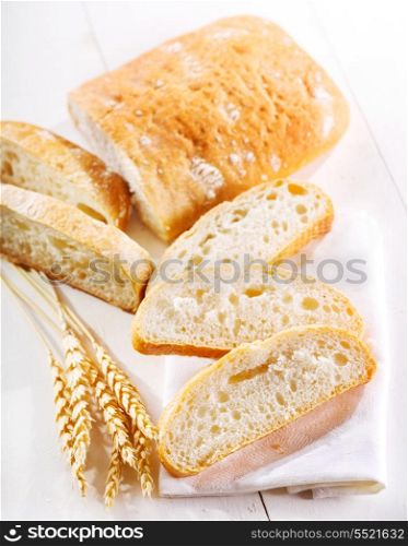 sliced ciabatta bread with wheat ears on wooden table