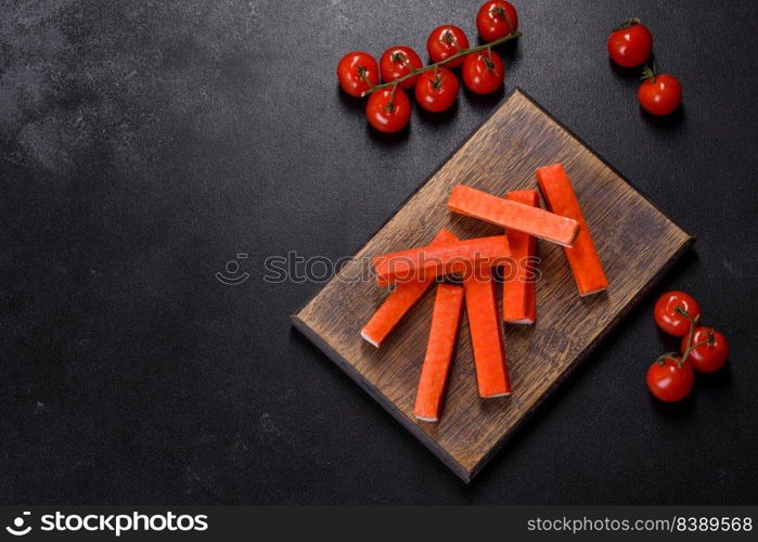 Sliced crab sticks on a cutting Board with a knife. On black rustic background. Crab sticks on a cutting Board with a knife. On black concrete background