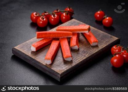 Sliced crab sticks on a cutting Board with a knife. On black rustic background. Crab sticks on a cutting Board with a knife. On black concrete background