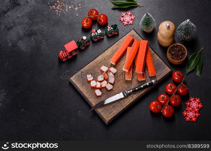 Sliced crab sticks on a cutting Board with a knife. On black rustic background. Crab sticks on a cutting Board with a knife. On a black christmas tab≤