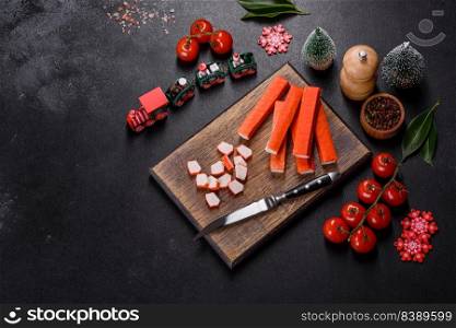 Sliced crab sticks on a cutting Board with a knife. On black rustic background. Crab sticks on a cutting Board with a knife. On a black christmas tab≤