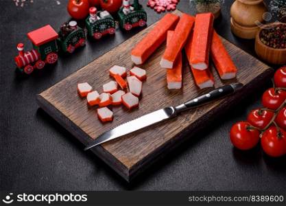 Sliced crab sticks on a cutting Board with a knife. On black rustic background. Crab sticks on a cutting Board with a knife. On a black christmas table