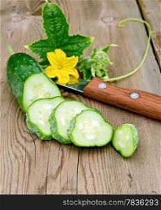 Sliced cucumber with yellow flower and green leaf, knife on a wooden board