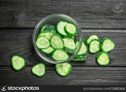 Sliced cucumbers in a glass bowl. On black wooden background. Sliced cucumbers in a glass bowl.