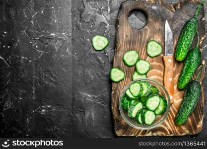 Sliced cucumbers on a cutting Board with a knife. On black rustic background. Sliced cucumbers on a cutting Board with a knife.