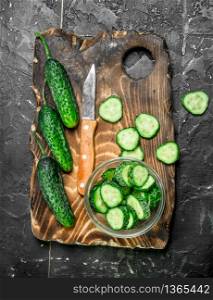 Sliced cucumbers on a cutting Board with a knife. On black rustic background. Sliced cucumbers on a cutting Board with a knife.