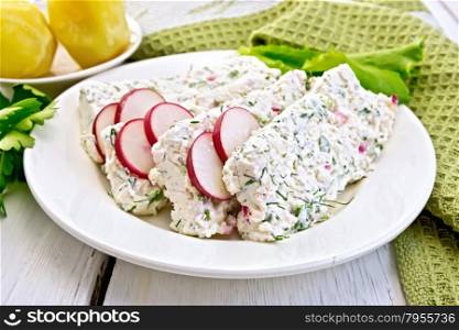 Sliced curd terrine with dill and radishes, green onions, salad on a plate, boiled potatoes, napkin, parsley on a light wooden planks