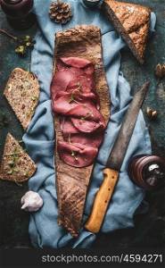 Sliced Deer meat ham with nut bread served on bark of tree with kitchen knife, top view