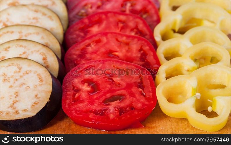 Sliced eggplant tomato and sweet pepper on wooden cutting board