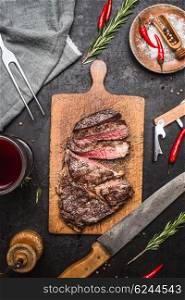 Sliced excellent medium rare grilled beef barbecue Sirloin steak on cutting board on rustic kitchen background with knife, spices and glass of red wine. Top view