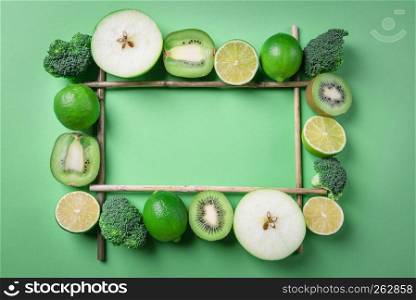 Sliced fresh fruits and vegetables displayed in a rectangular frame, on a green background. Dieting context. Detox food. Above view with copy space.