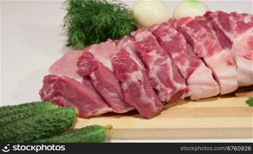 Sliced fresh pork meat and vegetables on wooden cutting board, close-up dolly shot