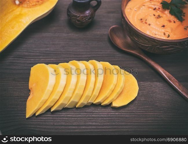 sliced fresh pumpkin and a plate with a thick pumpkin soup on a brown wooden background
