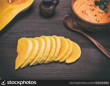 sliced fresh pumpkin and a plate with a thick pumpkin soup on a brown wooden background