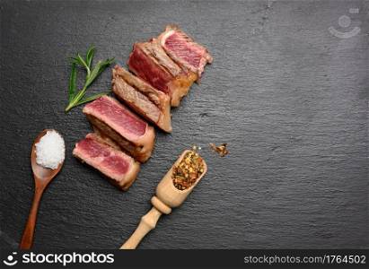 sliced fried beef steak New York striploin on a black background with spices, degree of doneness rare, top view, copy space