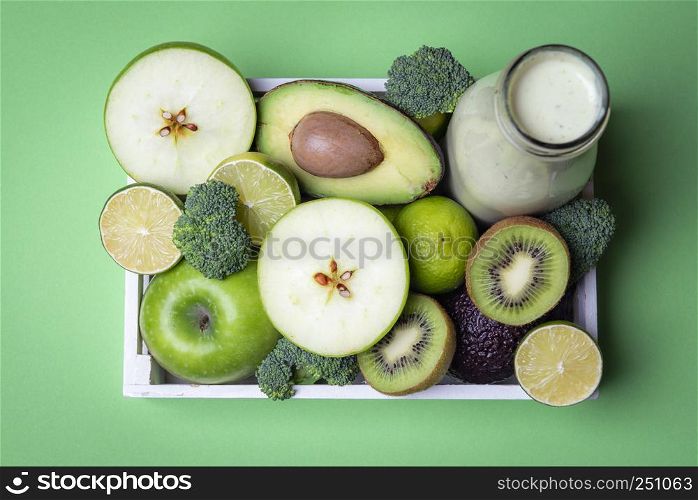 Sliced fruits and vegetables specific for detox diet and a bottle with smoothie. Green kitchen table above view
