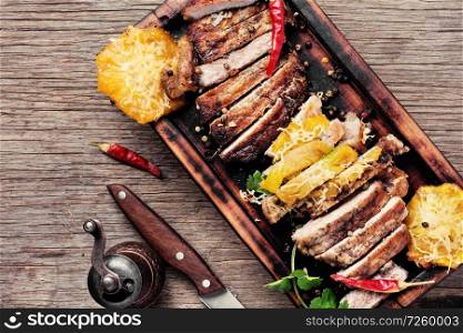 Sliced grilled roast meat with pineapple on wooden cutting board.American food. Juicy steak with pineapple