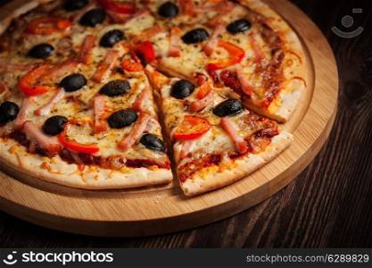 Sliced ham pizza with capsicum and olives on wooden board on table