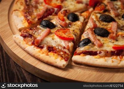 Sliced ham pizza with capsicum and olives on wooden board on table. Ham pizza