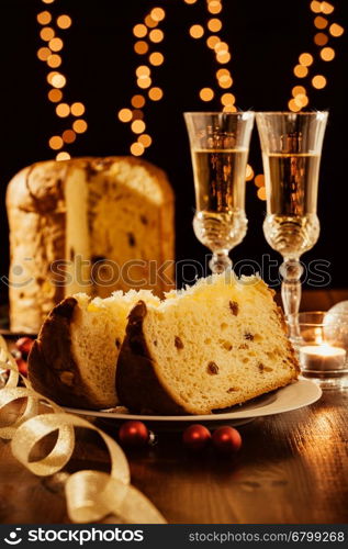 Sliced italian panettone, sparkling wine and decorations with Christmas lights on background