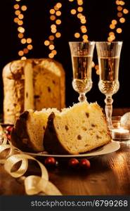 Sliced italian panettone, sparkling wine and decorations with Christmas lights on background