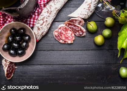 Sliced italian salami with green and black olives antipasti and red wine on black wooden background, top view, place for text. Italian food background
