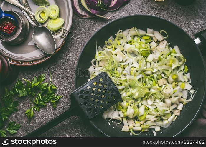 Sliced Leek in black frying pan on rustic kitchen table background, top view. Healthy vegetarian cooking and eating, diet food concept
