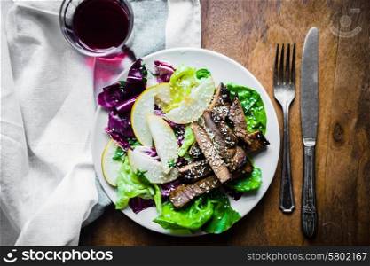Sliced meat steak with green salad and pears