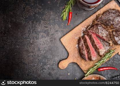 Sliced medium rare grilled steak on rustic cutting board with rosemary and spices , dark rustic metal background, top view, place for text