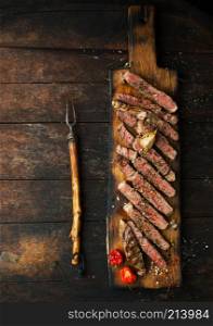 Sliced medium rare grilled steak ribeye with salt, spices, and rosemary on wooden cutting board